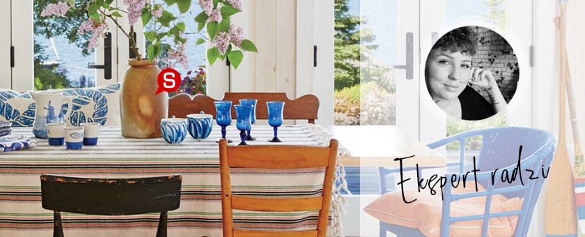 Przestronna jadalnia z dużymi oknami oraz stołem z wzorzystym obrusem. Na stole znajduje się wazon ze świeżym bzem oraz niebieskie dodatki. Przy stole stoją zaś drewniane krzesła.